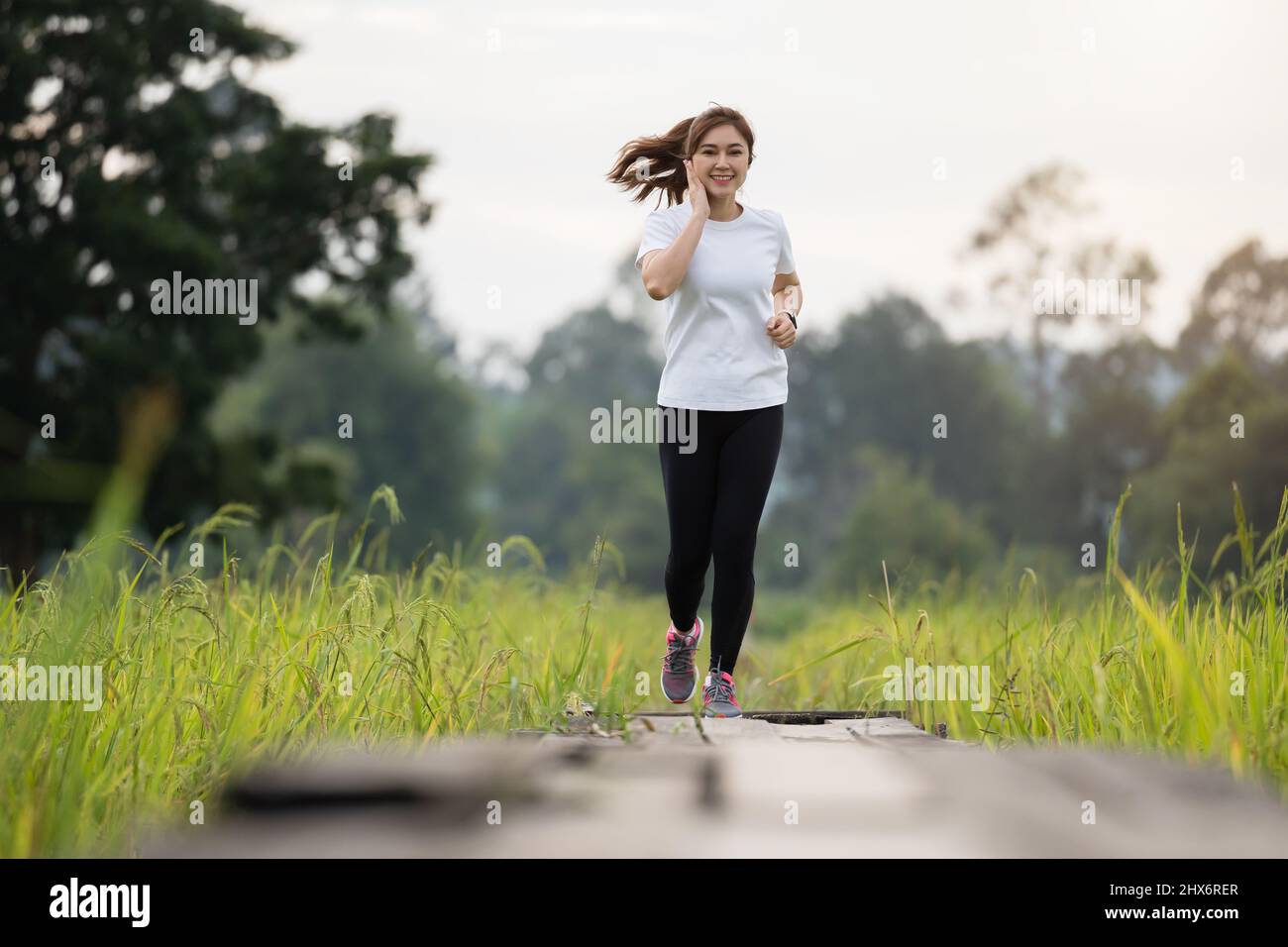 giovane donna che ascolta musica sulle cuffie mentre corre su un sentiero di legno nel campo Foto Stock