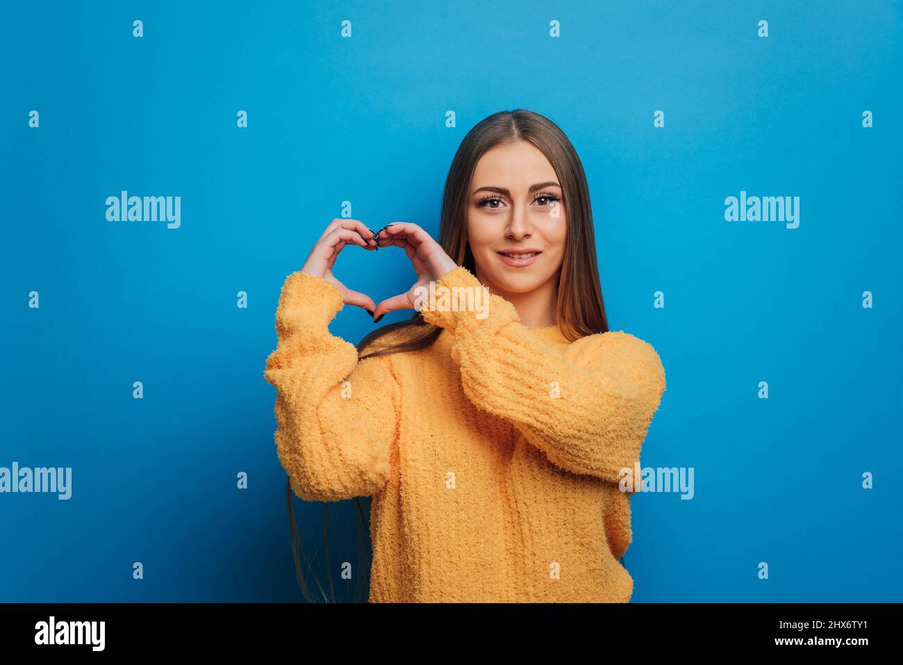 Donna che fa un cuore modellato con le mani mentre si alza su uno sfondo isolato. Foto Stock