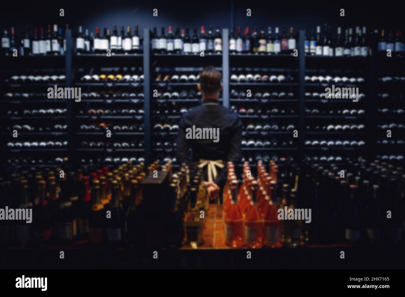 Sfondo sfocato per la degustazione, sommelier in piedi alla scaffale del vino in negozio di liquori. Foto Stock