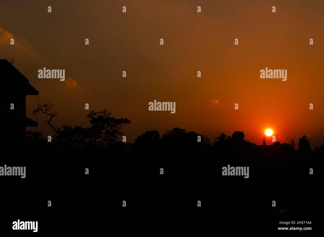 Silhouette di un edificio e gli alberi contro un sole tramonto. Foto Stock