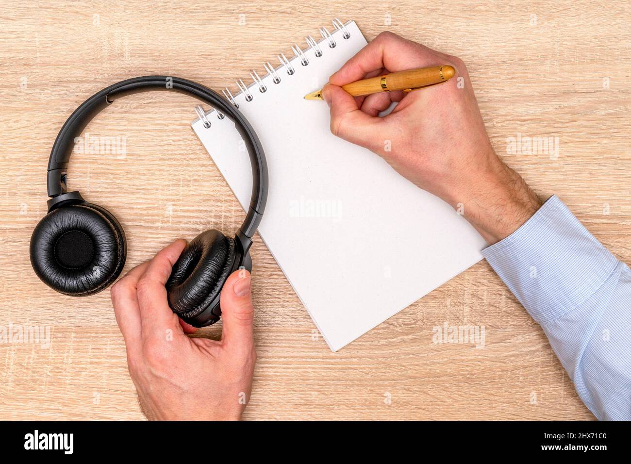 Mani maschili con un notebook e una penna, cuffie sul tavolo di legno, vista dall'alto Foto Stock