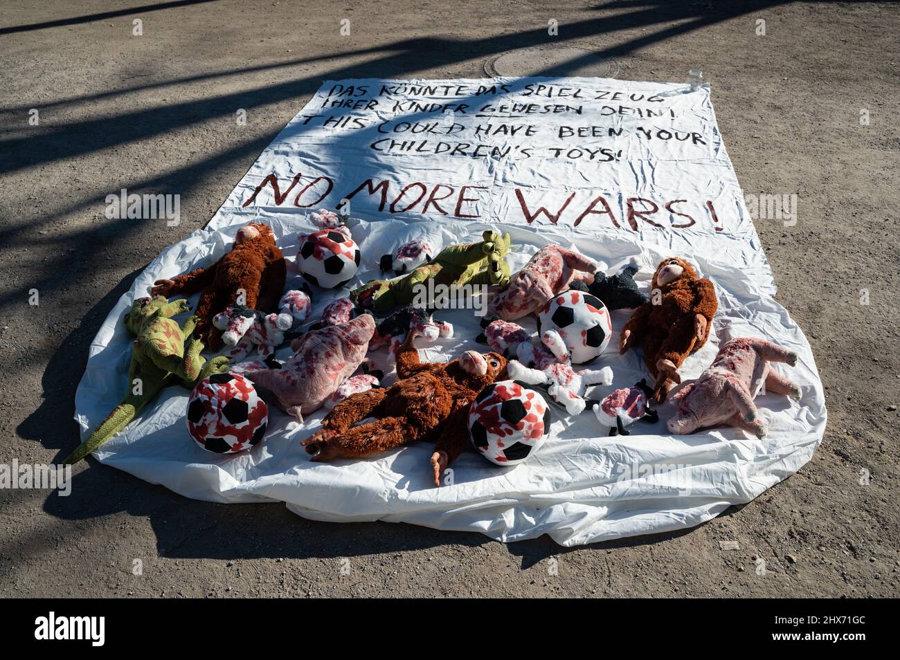 07.03.2022, Berlino, Germania, Europa - Installazione con giocattoli morbidi imbevuti di sangue su un banner come rappresentazione simbolica del numero di bambini morti. Foto Stock