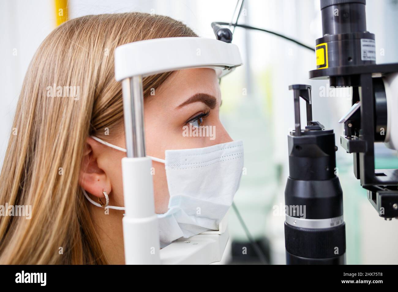 Giovane donna seduta in poltrona guardando la lampada a fessura durante l'esame medico negli occhi Foto Stock