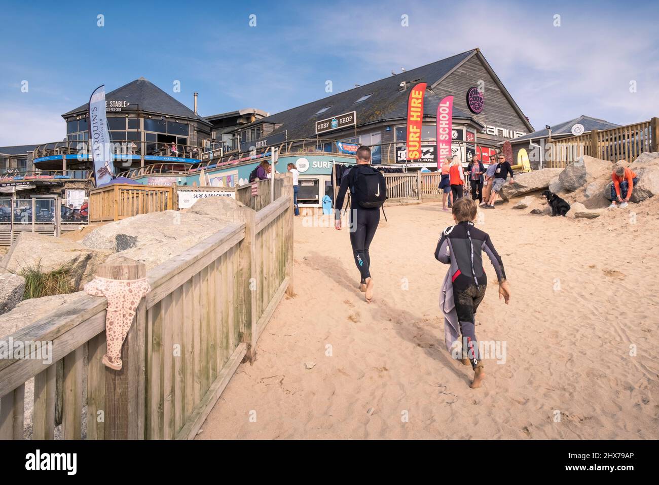I vacanzieri in mute che camminano fino al negozio di noleggio surf e al Fistral Beach Bar al Fistral a Newquay in Cornovaglia. Foto Stock