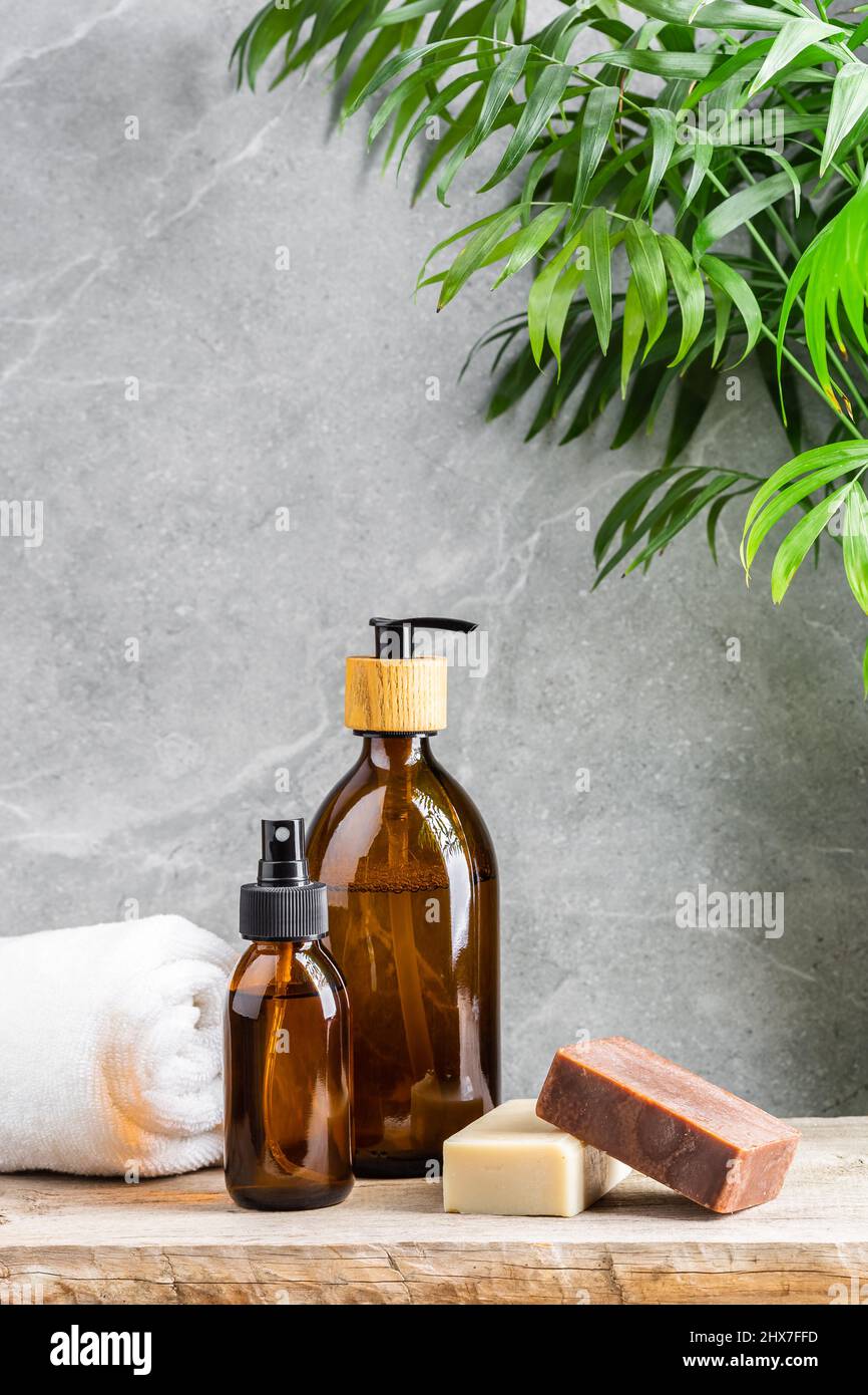 Tavolo da bagno con asciugamano bianco, bottiglie di vetro scuro con prodotti per la cura della pelle liquida e saponette naturali fatte a mano su sfondo di marmo grigio e Foto Stock