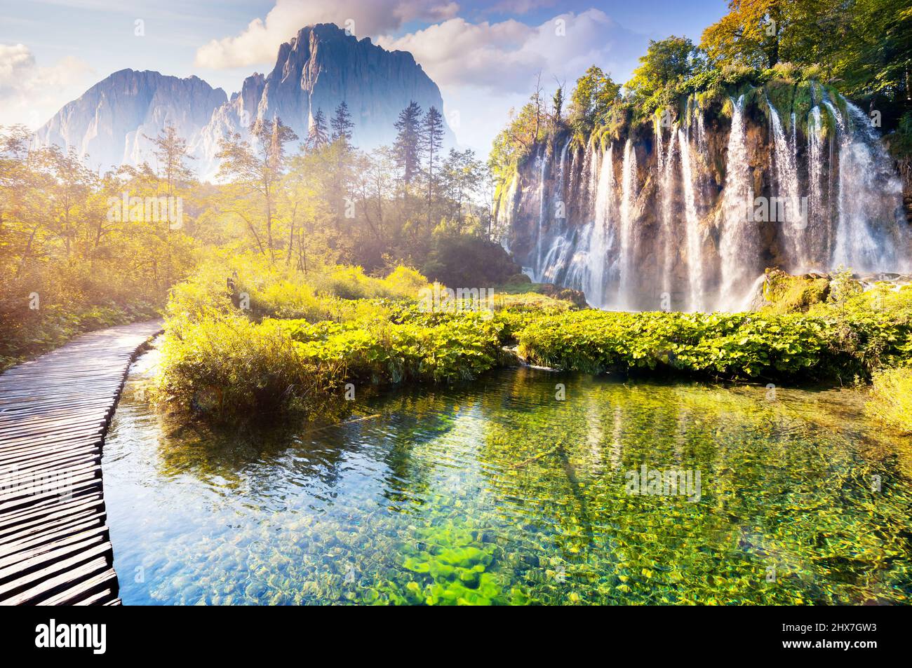 Vista maestosa sulla cascata con acque turchesi e travi soleggiate nel Parco Nazionale dei Laghi di Plitvice. Foresta che brilla dalla luce del sole. Croazia. Europa. DRAM Foto Stock