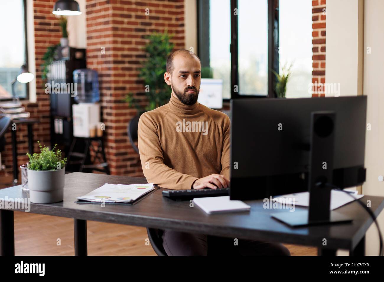 Giovane project manager che lavora su grafici finanziari mentre si siede alla scrivania utilizzando il computer di lavoro. Consulente aziendale di marketing brainstorming idee di investimento e ricerca statistiche di gestione. Foto Stock
