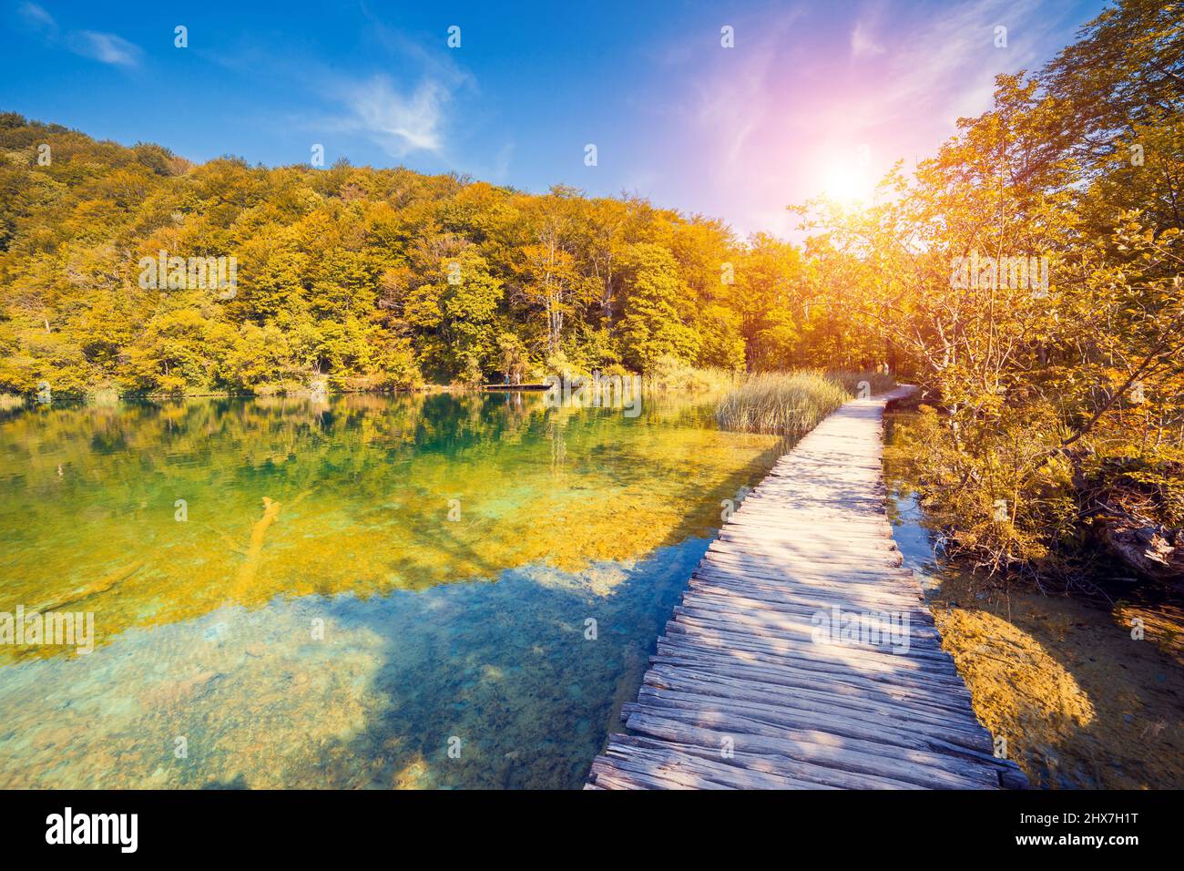 Vista maestosa sulla cascata con acque turchesi e travi soleggiate nel Parco Nazionale dei Laghi di Plitvice. Foresta che brilla dalla luce del sole. Croazia. Europa. DRAM Foto Stock