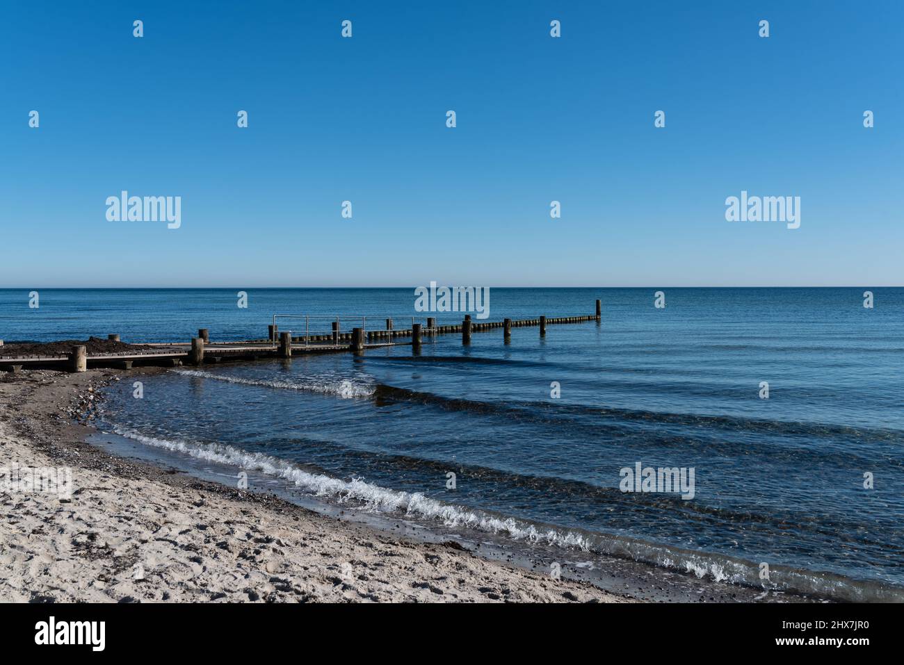 spiaggia di sabbia del mar baltico con molo da bagno e frangiflutti di legno contro il cielo blu chiaro Foto Stock