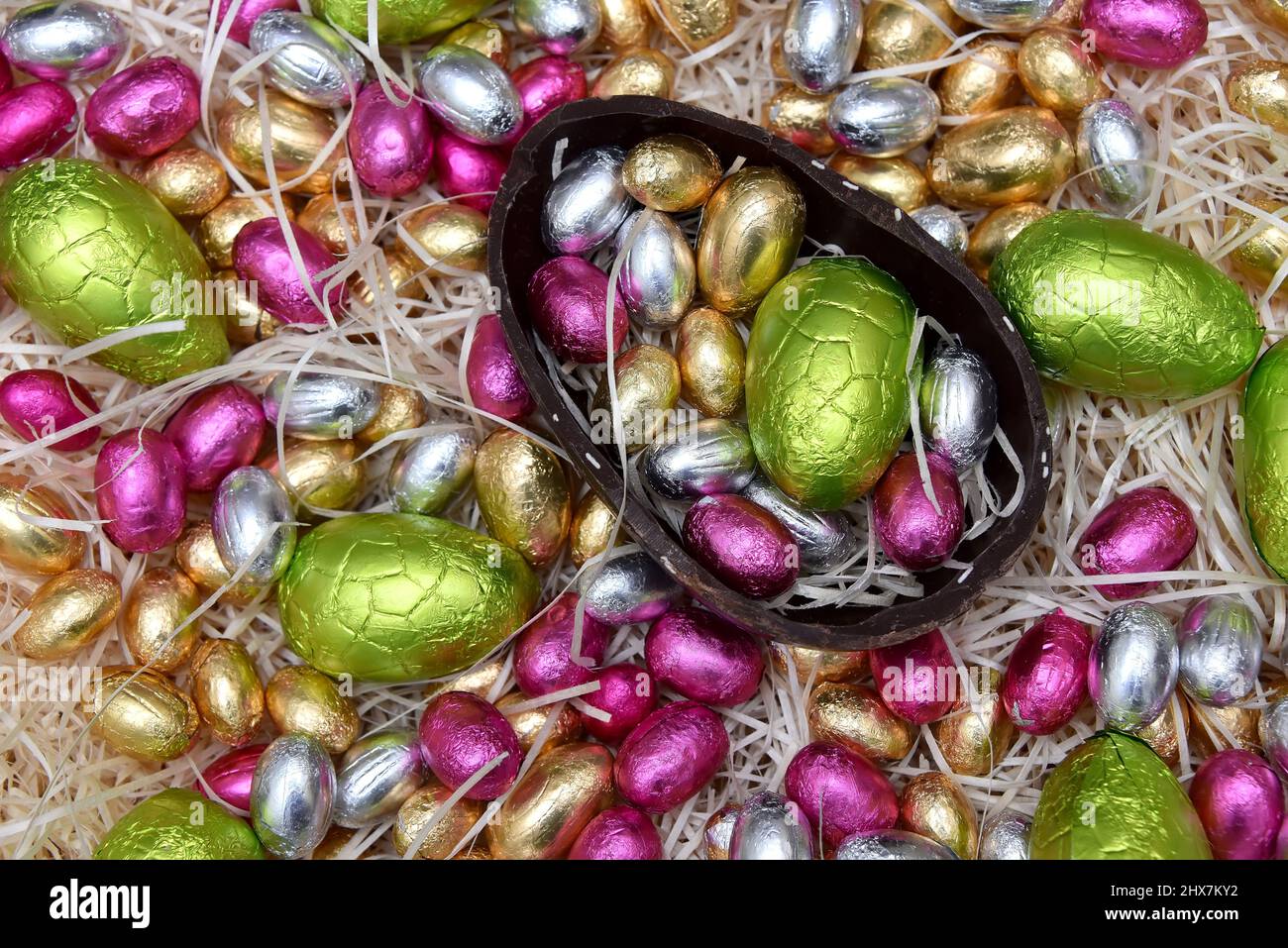 Mucchio di coloratissimi fogli di cioccolato uova di pasqua in verde, rosa, giallo e oro con metà di un grande uovo di cioccolato marrone scuro. Foto Stock