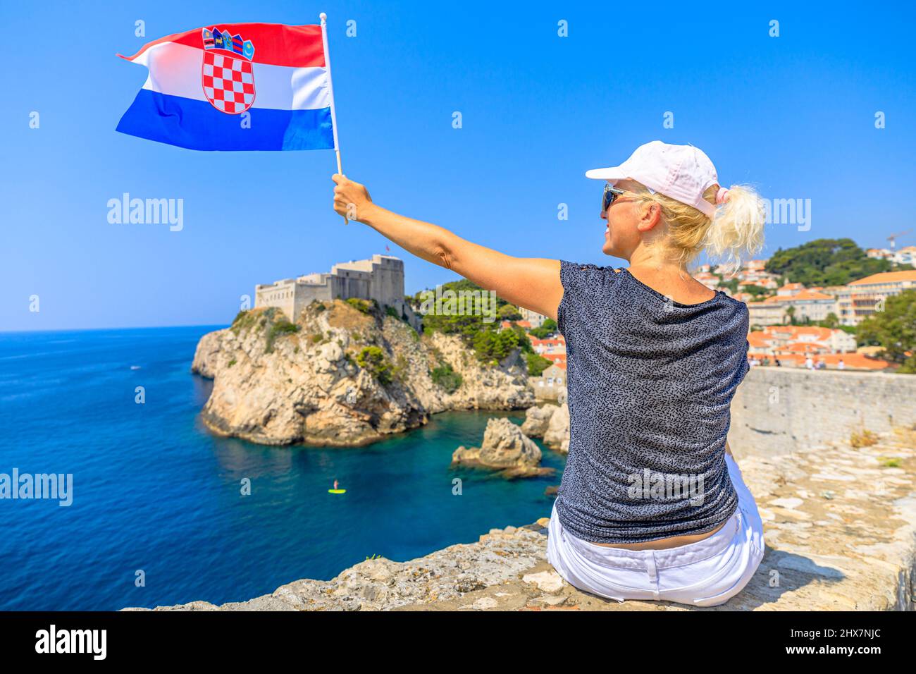 Donna con bandiera croata sulle mura croate di Dubrovnik. Vista sulla fortezza di Fort Lovrijenac e sul porto occidentale. Dubrovnik, patrimonio mondiale dell'UNESCO Foto Stock