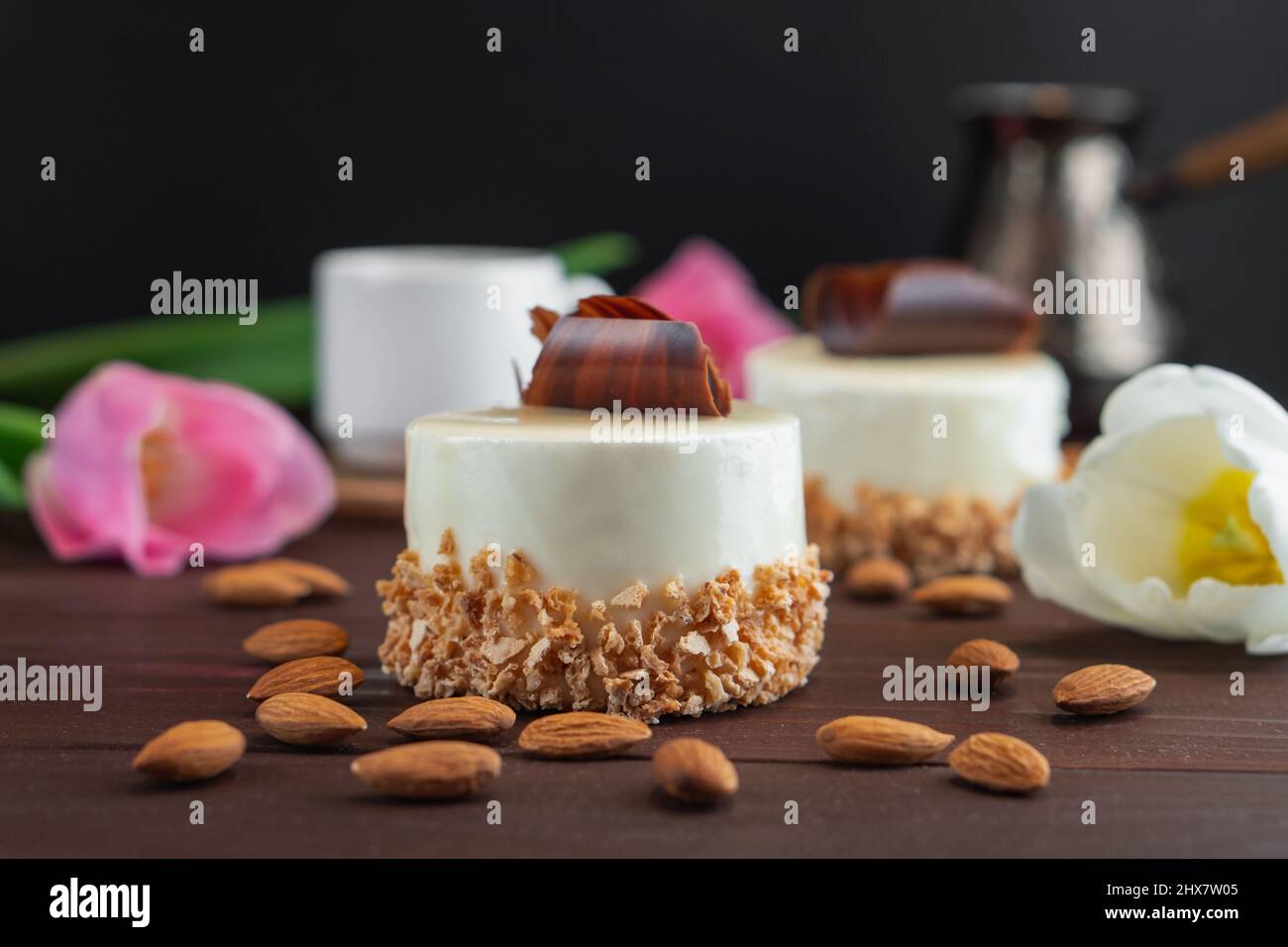 Due cupcake con tazza di caffè bianco al cioccolato, mandorla e tulipani su un tavolo di legno. Messa a fuoco selettiva Foto Stock