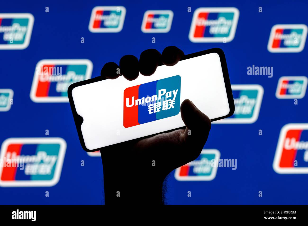 UnionPay è un sistema di trasferimento di denaro elettronico cinese in tutto il mondo. Logo UnionPay sullo schermo dello smartphone in mano appiciata sullo sfondo dei logo UnionPay. Foto Stock