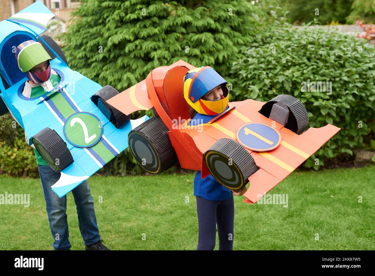 Bambini che indossano modelli di auto da corsa in cartone/costume, giocando in giardino Foto Stock
