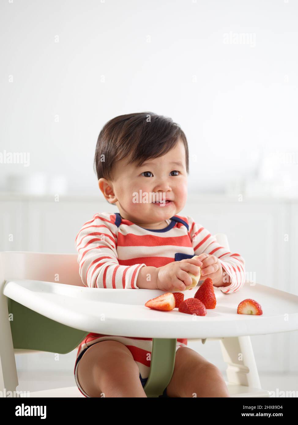 Bambino di 11 mesi che mangia in seggiolone Foto Stock