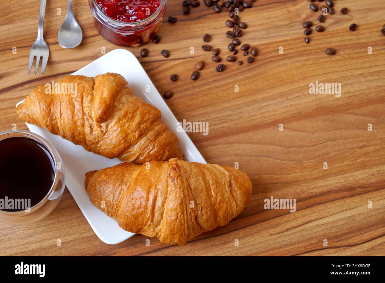 Su un piatto rettangolare bianco ci sono due croissant per la colazione. Nelle vicinanze troverete anche marmellate e caffè. Foto Stock