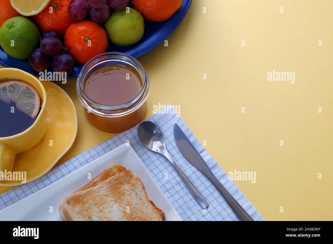 sfondo giallo soleggiato migliora l'appetito. Una colazione a base di pane tostato con marmellata o miele, tè e frutta è il modo migliore per iniziare la giornata. Foto Stock