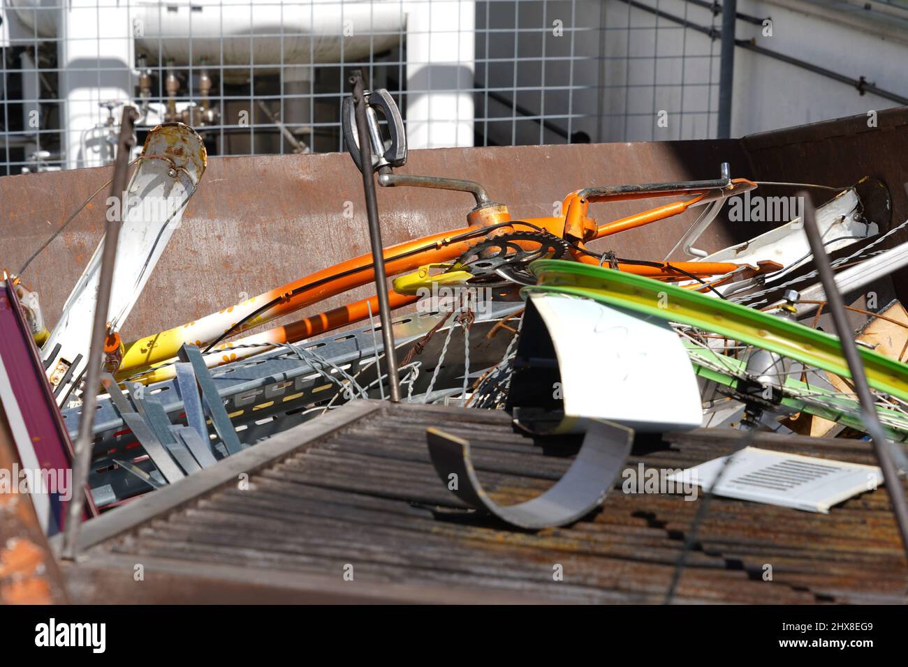 Rifiuti di metalli vari e misti raccolti in un contenitore in un luogo di smaltimento comunitario di fronte all'edificio bianco. Servizio pubblico gratuito Foto Stock