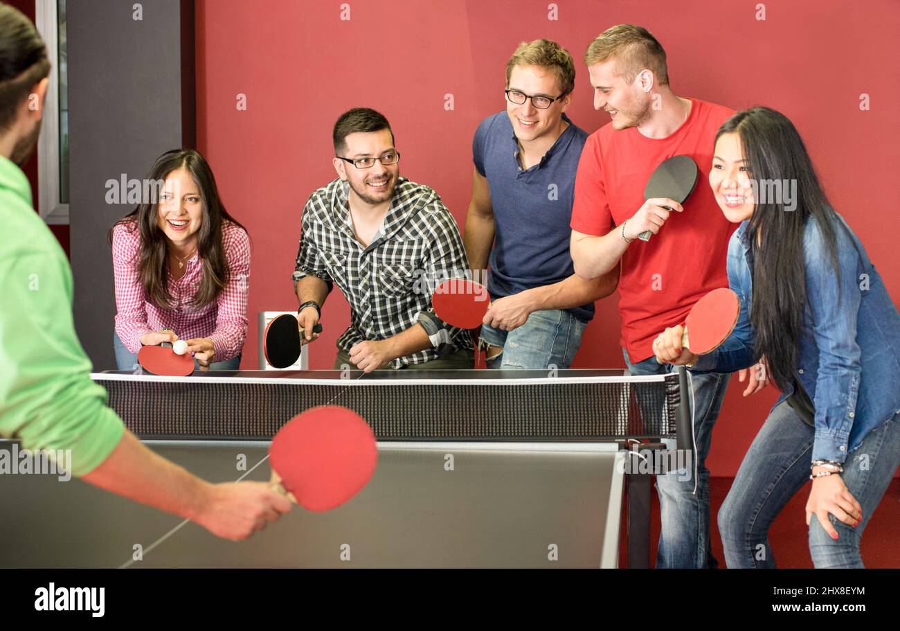 Gruppo di giovani amici felici che giocano a ping pong ping pong ping pong - momento di divertimento in sala giochi del viaggiatore ostello della gioventù - concetto di sport d'epoca e genuino Foto Stock