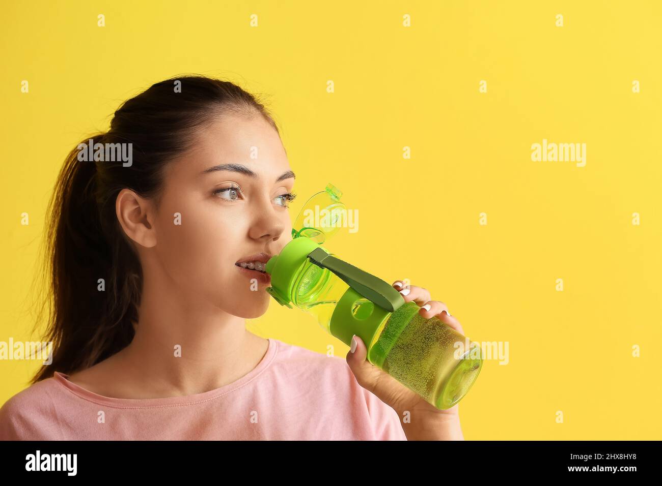 Ragazza adolescente sportiva bere acqua su sfondo giallo Foto Stock