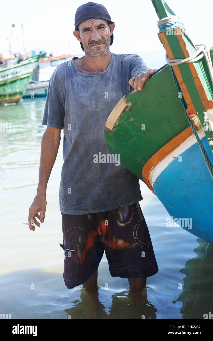 Essere un pescatore può essere duro. Ritratto di un pescatore in piedi in acque poco profonde accanto alla sua barca. Foto Stock