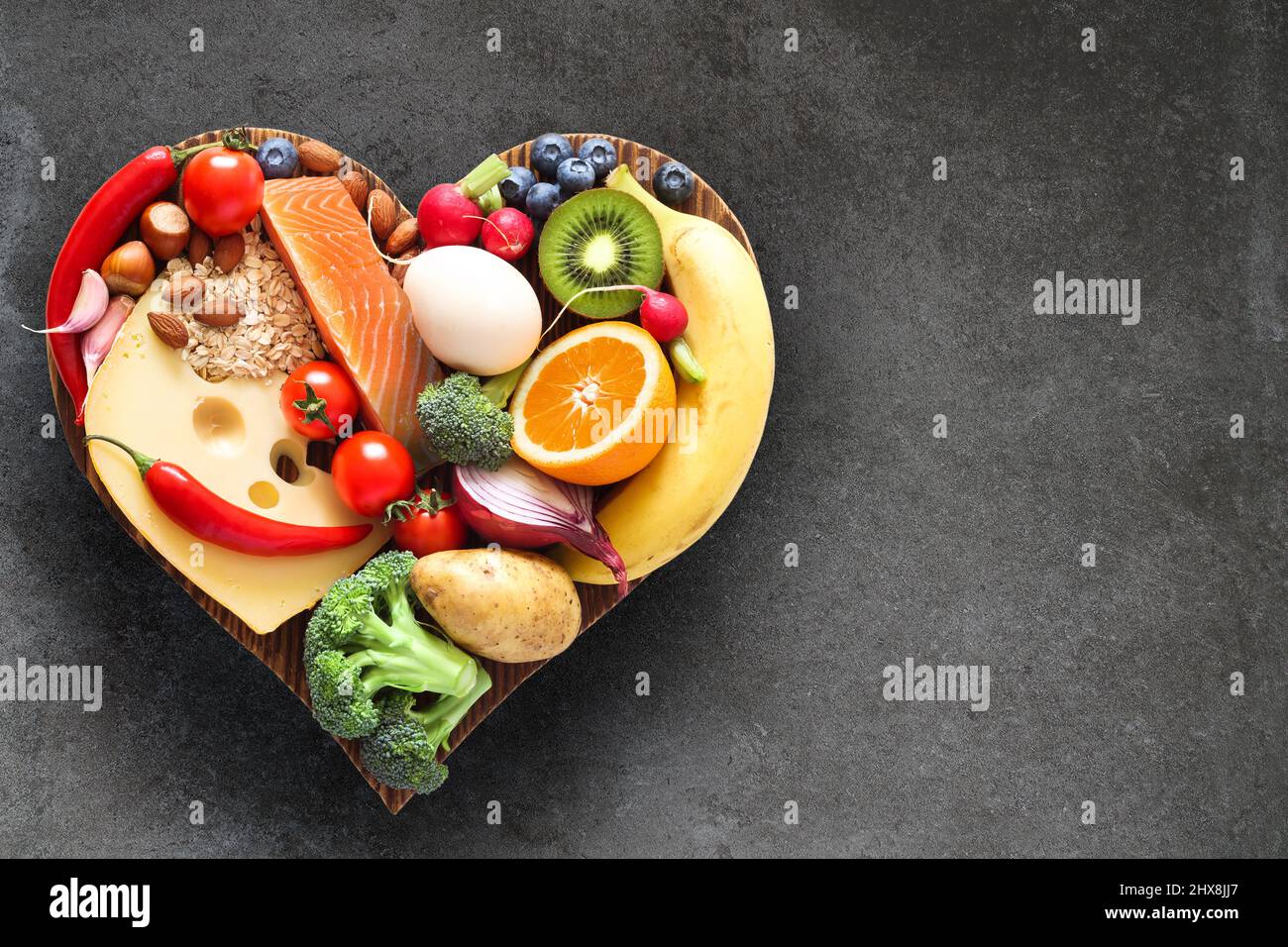 Dieta equilibrata. Cibo sano su un tagliere di legno a forma di cuore. Foto Stock