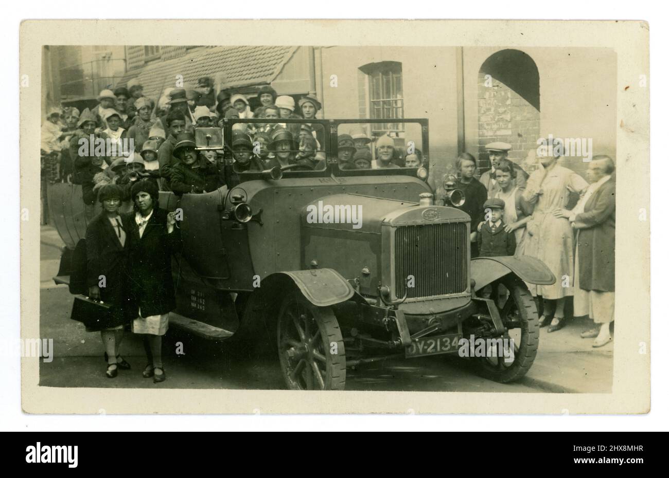 Originale 1920's cartolina charabanc, sembra essere un bambino compleanno festa, o giorno speciale fuori, come alcuni stanno portando cappelli di partito, molti bambini crammed nel charabanc, con i loro genitori, onlookers sulla strada. Brighton, Sussex, Inghilterra, Regno Unito Foto Stock