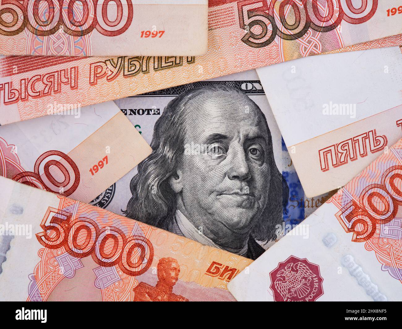 Un conto di cento dollari sotto circa cinquemila banconote rubli. Primo piano. Foto Stock