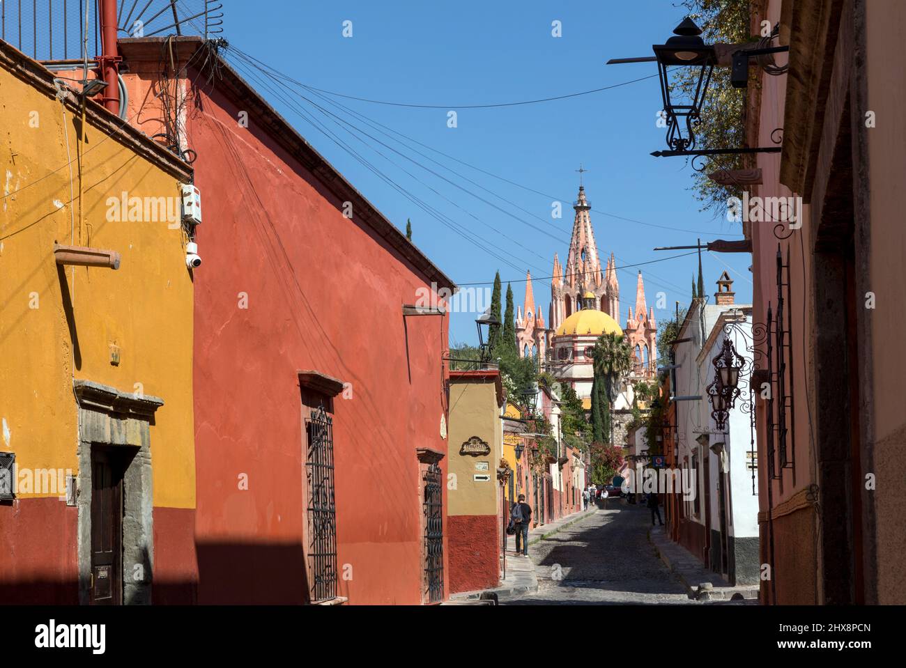 Messico, Guanajuato, San Miguel de Allende, una strada laterale della città con case e negozi che conduce in città con Parroquia de San Miguel Arcángel Foto Stock