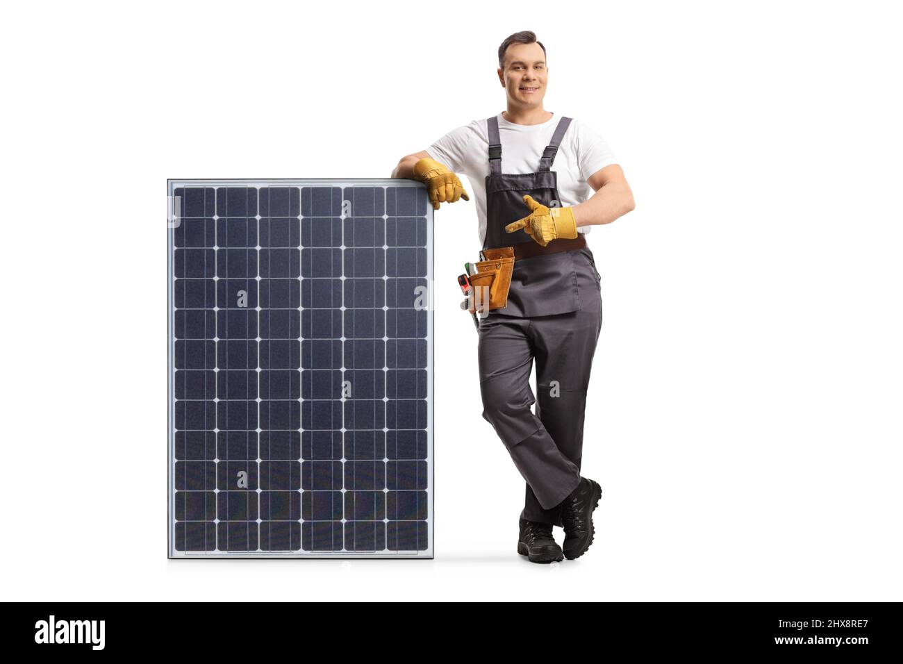 Uomo in uniforme appoggiandosi su un modulo fotovoltaico per l'energia solare sostenibile e puntando isolato su sfondo bianco Foto Stock