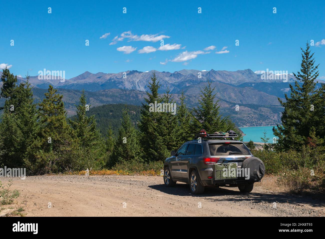 Guidare le strade secondarie tra le montagne della Columbia Britannica. Auto equipaggiata per il fuoristrada in primo piano con lago e montagne sullo sfondo Foto Stock