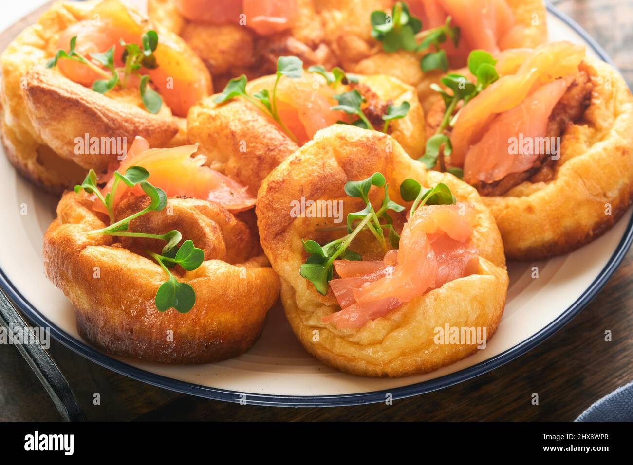 Budino dello Yorkshire. Tradizionale budino inglese dello Yorkshire con contorno di salmone e ravanello con microgreens su piatto bianco e tavolo di fondo grigio chiaro. Foto Stock