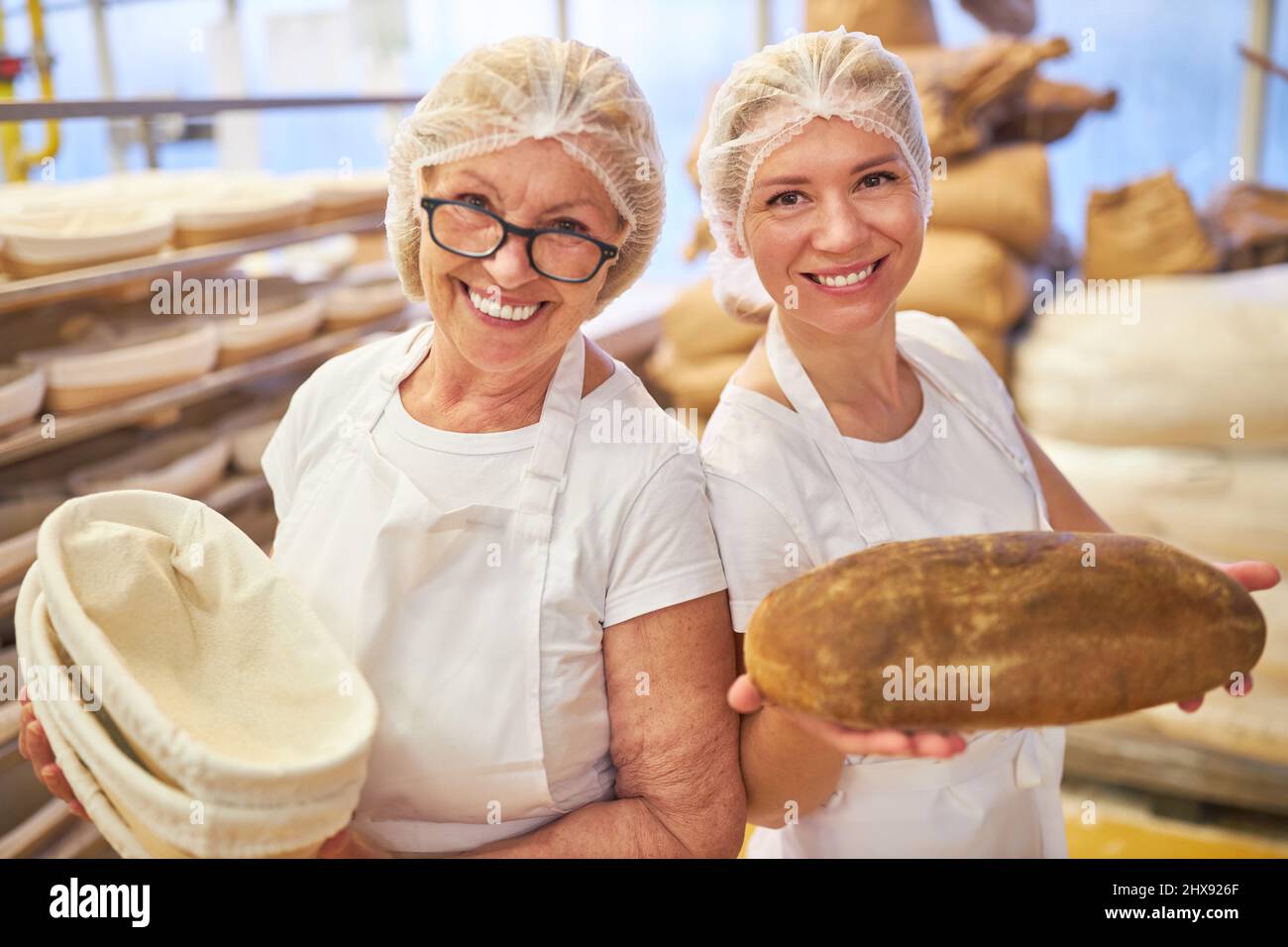 Due donne nel team di panetteria con panieri e una pagnotta fresca di pane nel grande panificio Foto Stock