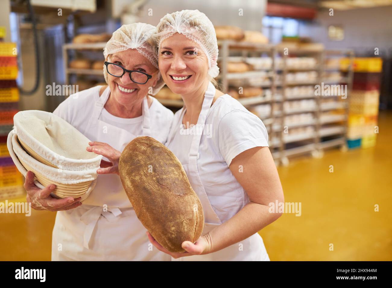 Giovane donna panettiere apprendista e panettiere senior con una pagnotta di pane in una grande panetteria Foto Stock