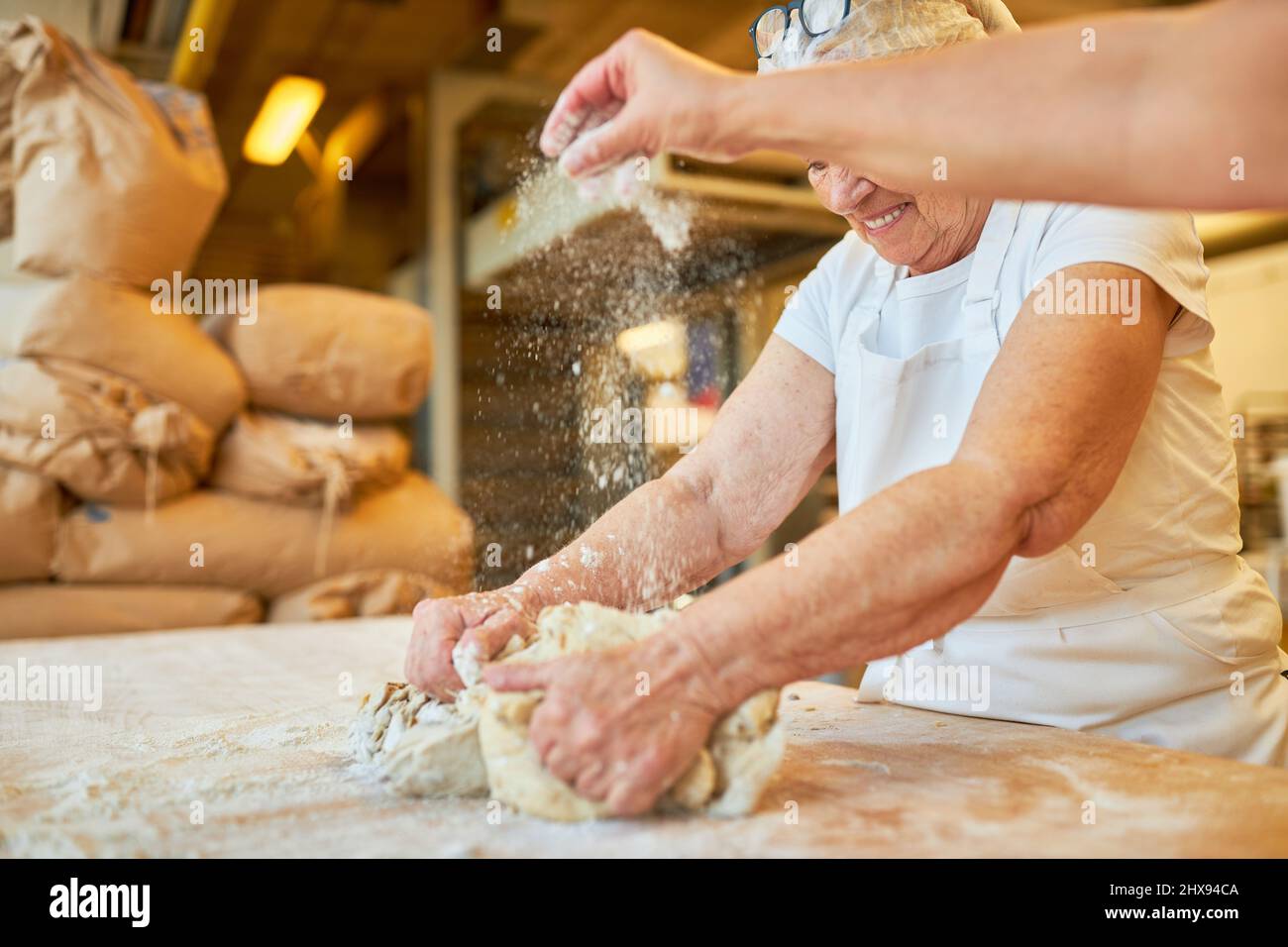 Due panettieri impastano l'impasto e spolverano la farina per preparare la cottura in una squadra in una panetteria Foto Stock