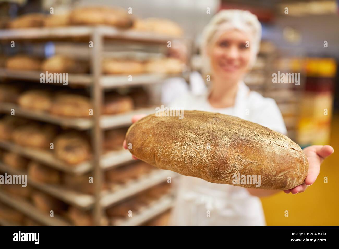 L'apprendista panettiere è orgogliosa di presentare una pagnotta di pane appena sfornata con scaffale in sottofondo Foto Stock