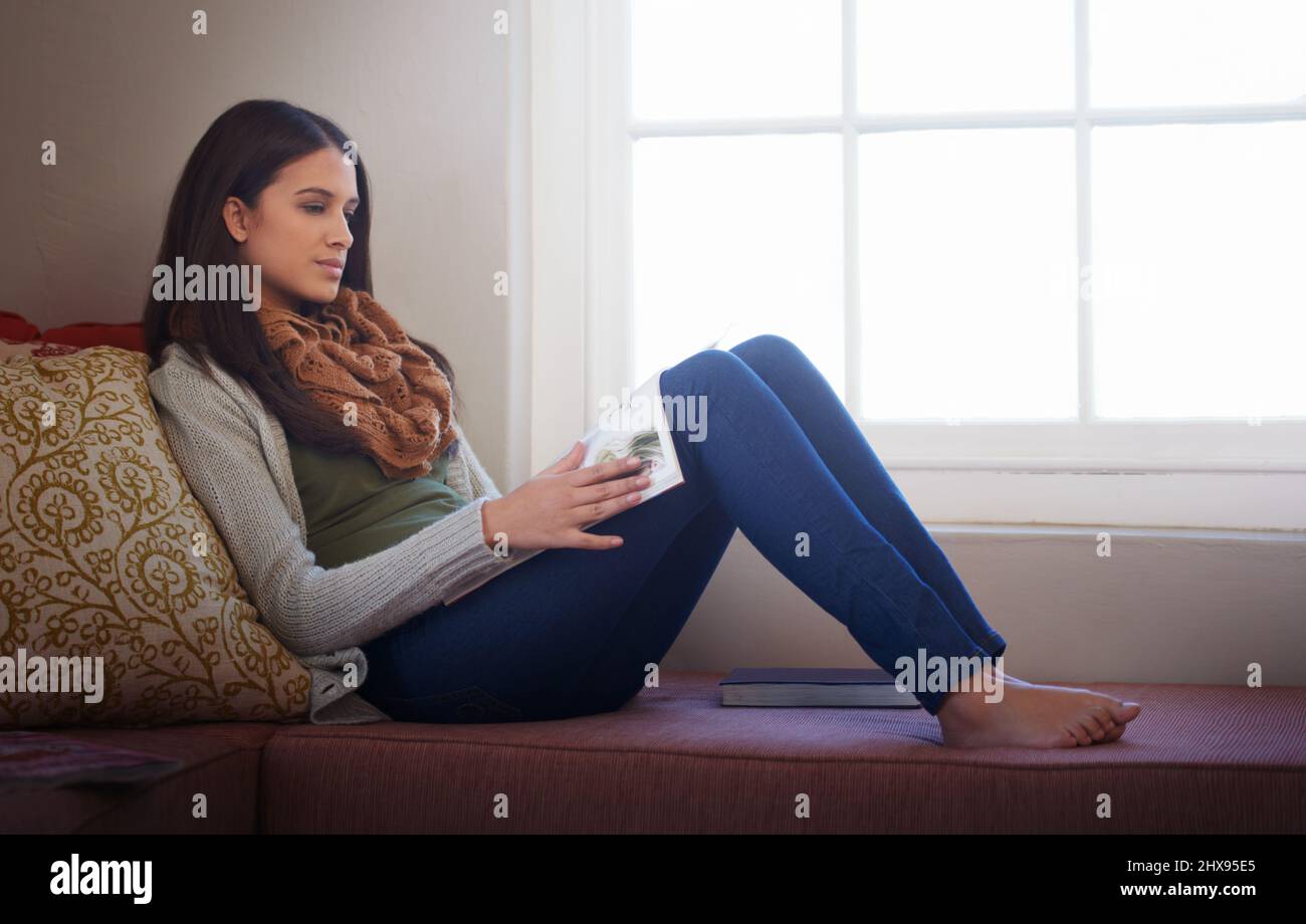 Leggere un interessante articolo. Una giovane donna che legge un libro a casa. Foto Stock
