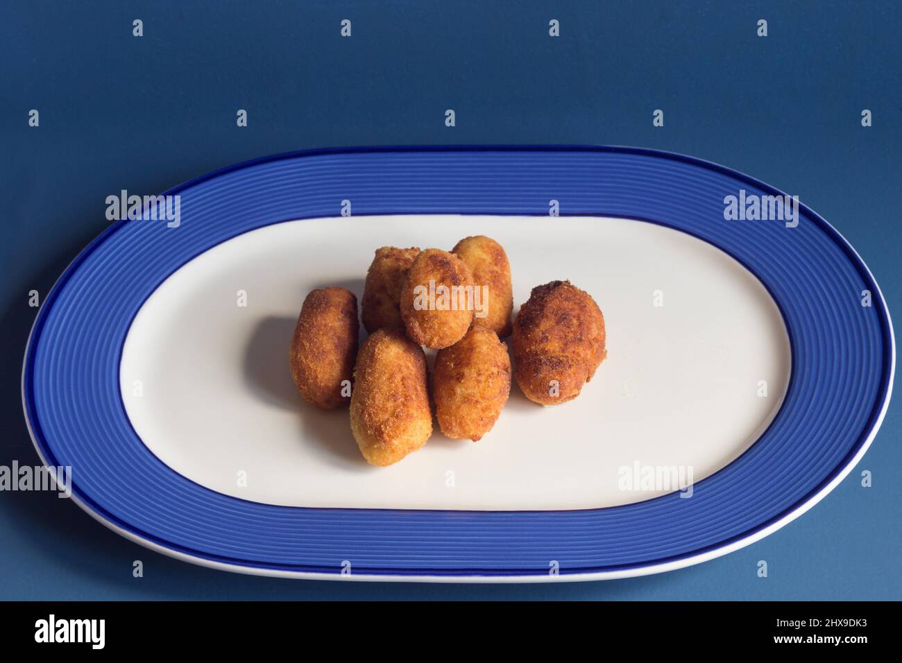 Un mazzo di crocchette su un piatto decorato con linee geometriche su sfondo blu studio. Stoviglie e cibo. Foto Stock