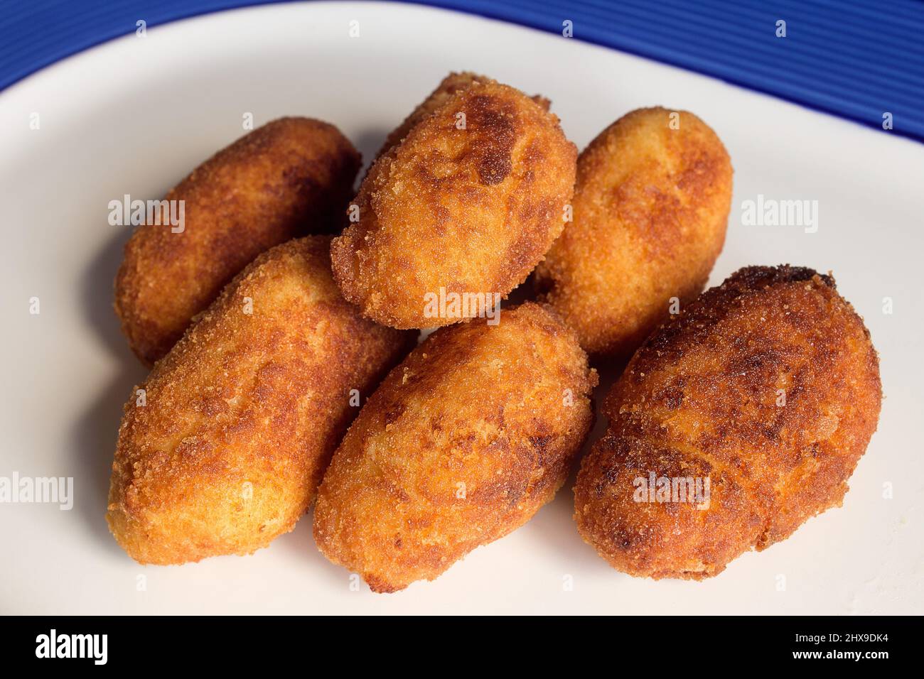 Un gruppo di crocchette dorate fritte su un piatto decorato con linee blu. Texture e cibo. Foto Stock