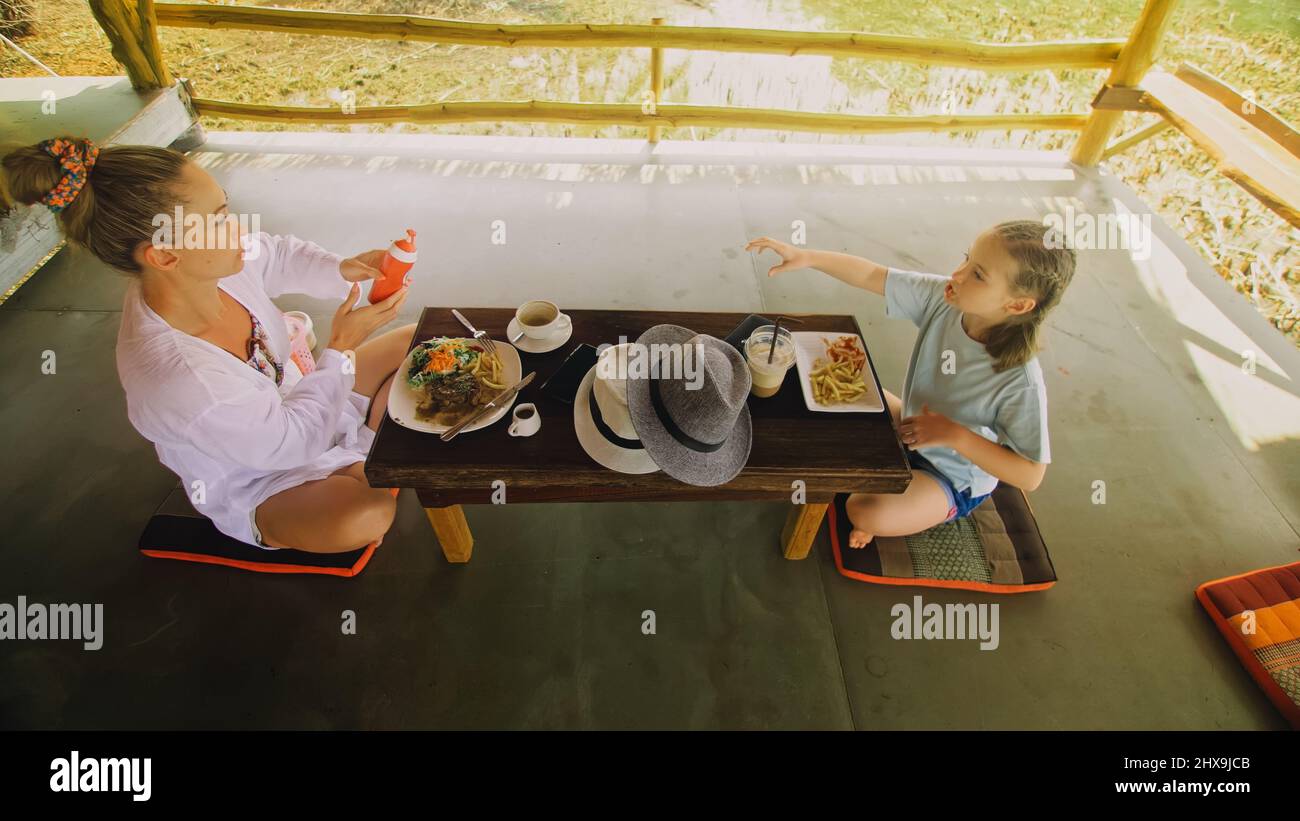 La famiglia Happy mangia e beve gustose bevande trascorrendo del tempo in un locale caffè galleggiante sull'acqua. Madre e figlia che hanno la colazione all'aperto. Donna e. Foto Stock