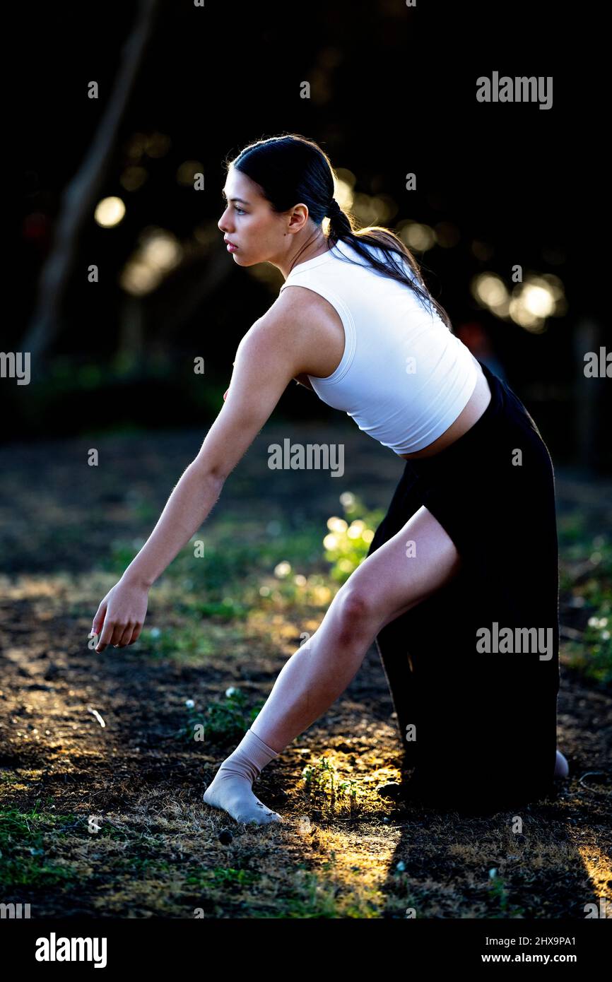 Giovane ballerina multirazziale femmina nel boschetto di alberi cipressi Foto Stock