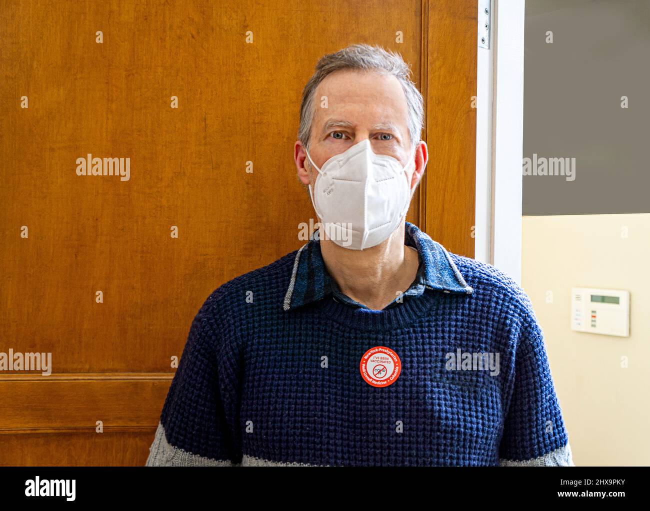 Maschera protettiva per il viso uomo con adesivo di vaccinazione COVID-19 sul maglione Foto Stock