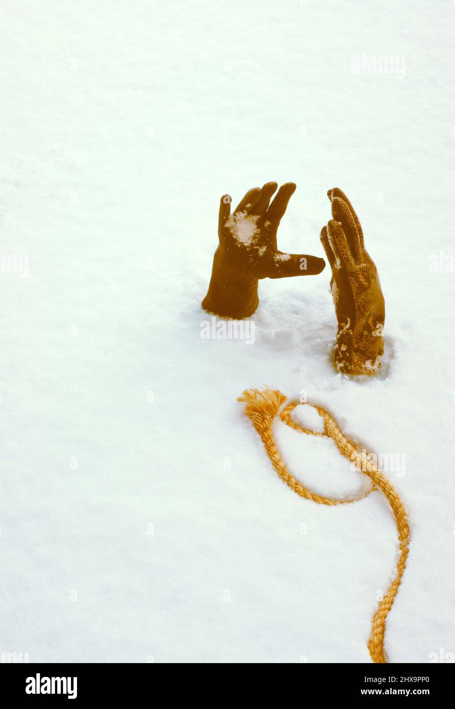 Le mani coperte si allungano e si sgommano dalla neve come se la persona fosse sepolta. Una corda si estende attraverso la neve per aiutare e aiutare come un'ancora di salvezza. Spazio di testo. Foto Stock