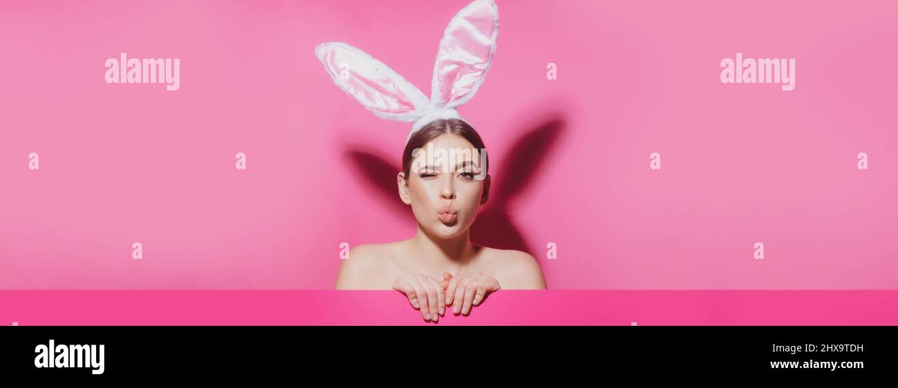 Banner di Pasqua con donna conigliata. Primo piano ritratto di attraente ragazza allegra indossando orecchie rosa, bacio d'aria. Donna coniglietto di Pasqua. Foto Stock