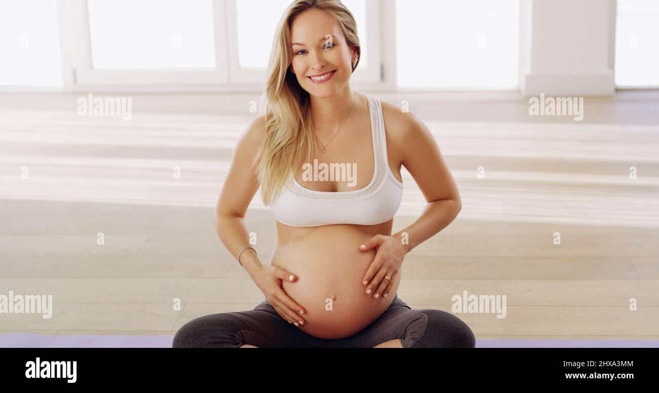 Rimanere in salute per il bambino. Ritratto corto di una giovane donna incinta attraente strofinando il suo bump del bambino mentre si siede su un tappeto di yoga. Foto Stock