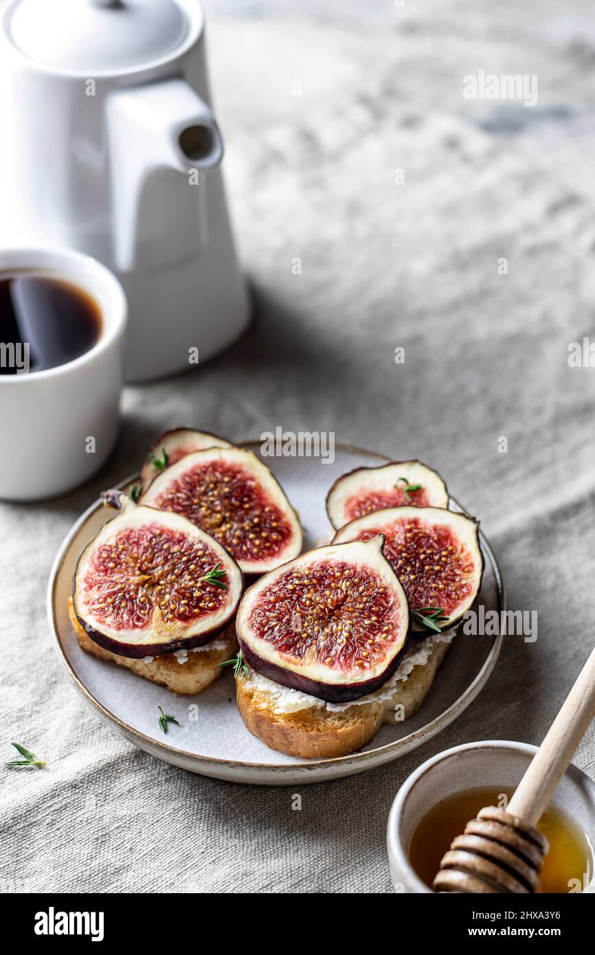 Due sandwich con fichi, timo su sfondo testurizzato. Composizione colazione con caffè, miele, tovagliolo di lino. Orientamento verticale. Primo piano Foto Stock