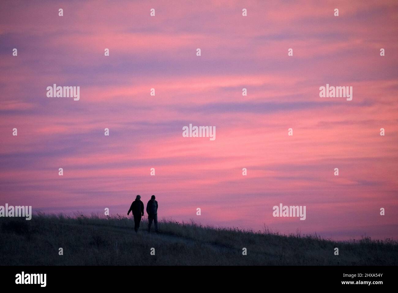 Donna e uomo che camminano lungo un sentiero all'aperto in un parco naturale di prati con cielo rosa al tramonto. Foto Stock