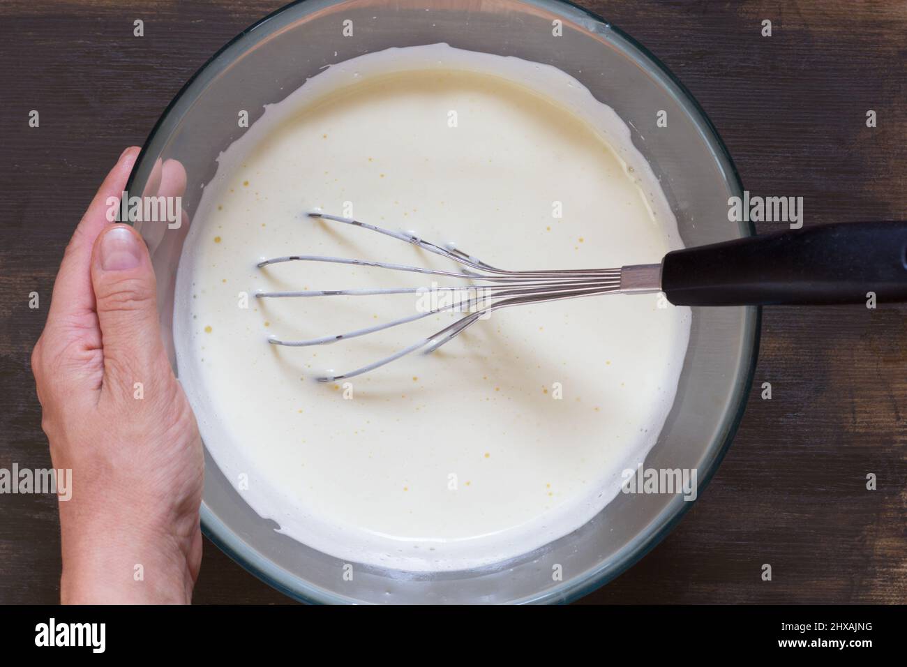 Donna che tiene la ciotola di vetro con le uova sbattute e frusta in esso Foto Stock