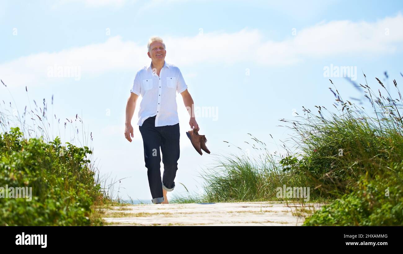 Camminando a piedi nudi attraverso il parco. Un uomo anziano che cammina attraverso un parco con le sue scarpe in mano. Foto Stock