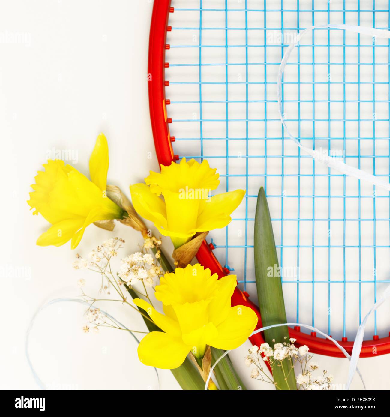 Tennis. Composizione sportiva per le vacanze con racchetta da tennis con bouquet di narcisi su sfondo bianco. Sport e stile di vita sano. Il concetto di outd Foto Stock